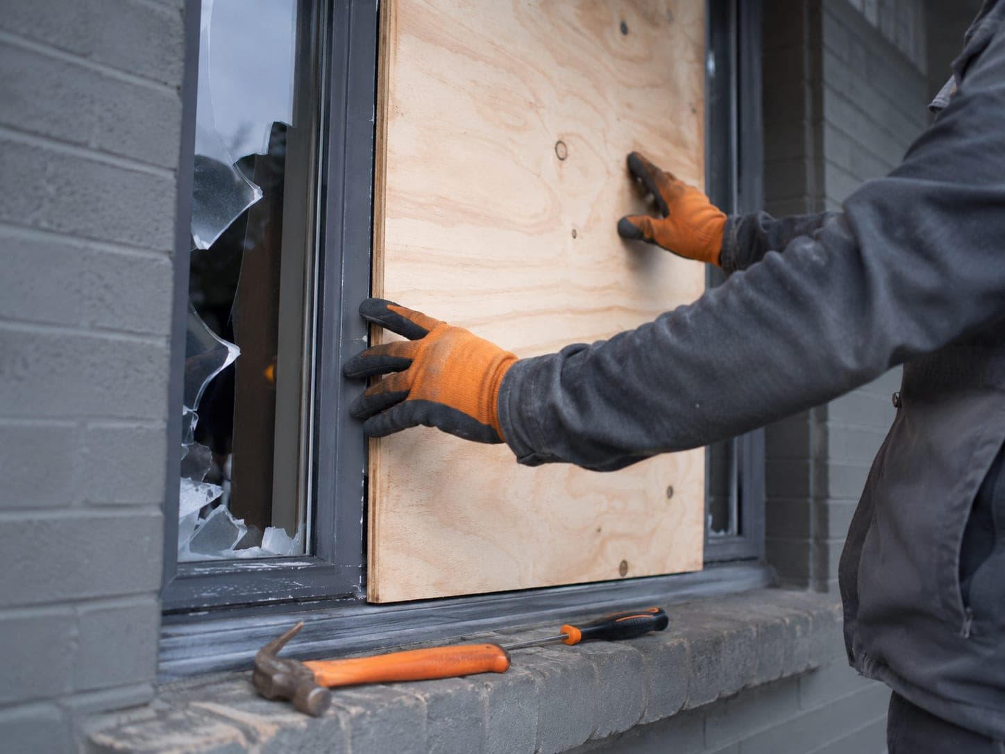 Technician securing a broken house window on site, with tools and a hazard light